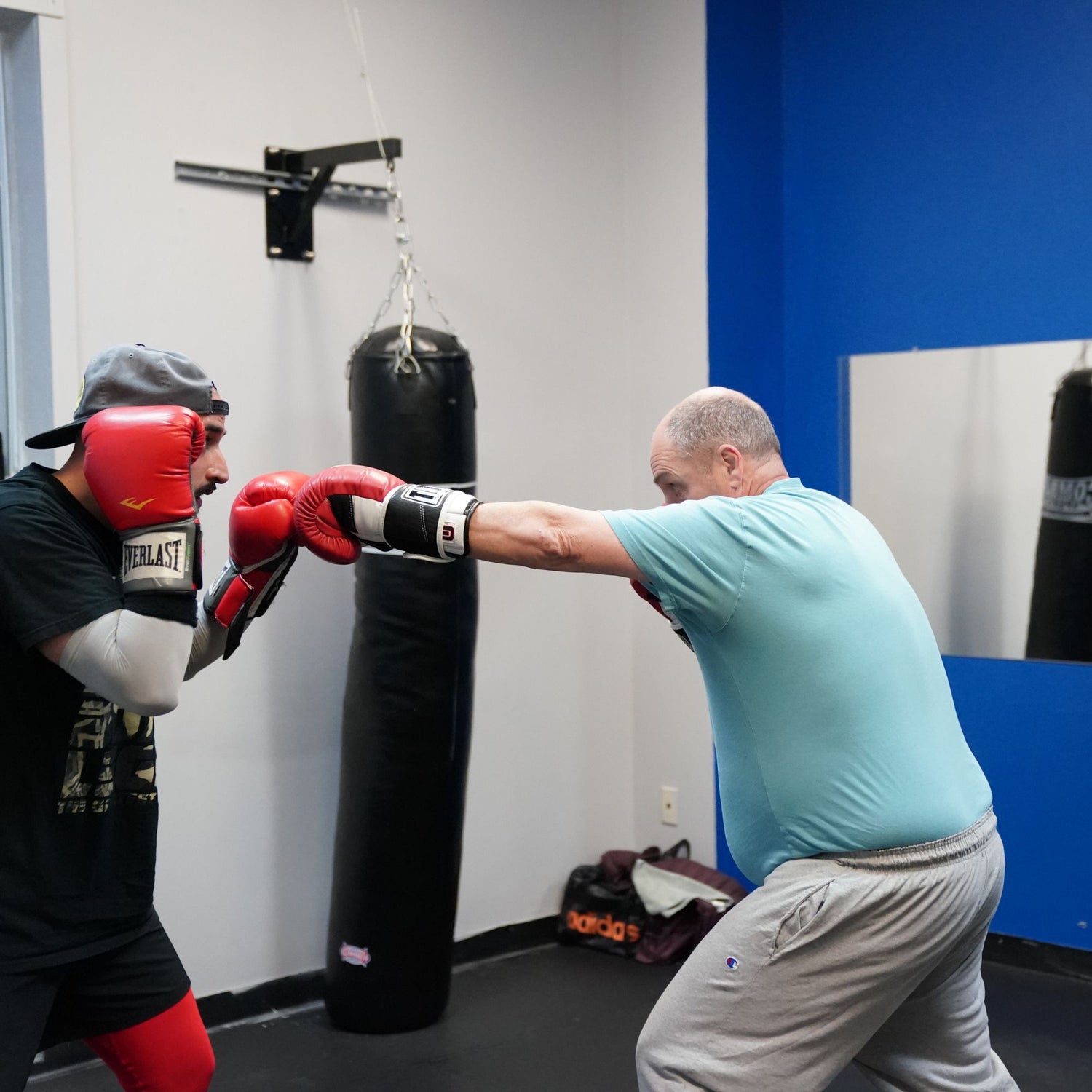 Man in blue shirt throwing a jab at another man in a black shirt within a boxing gym 